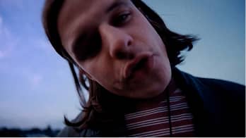 Close-up of a person with long hair wearing a striped shirt and blowing a kiss.