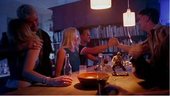 Group of friends fist-bumping and socializing in a dimly lit room with drinks on a bar counter.