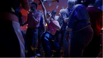 Group of people dancing and enjoying at a dimly lit party or club with colorful lights.