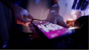 Person holding a credit card near a smartphone with a bright screen in a dimly lit setting.