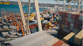 Large shipping port with stacked cargo containers and cranes near a body of water.