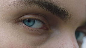 Close-up of a blue eye with thick dark eyebrow and light skin.