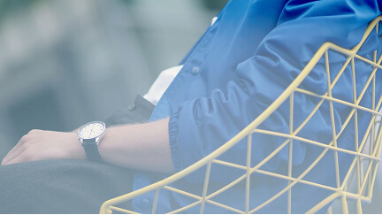 Person wearing a blue jacket sitting on a yellow wireframe chair, with a wristwatch visible.