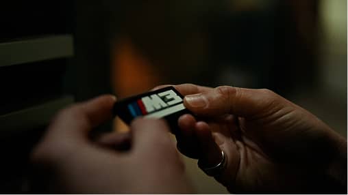 Hands holding a BMW M car emblem badge with blurred background in low light.