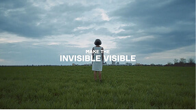 Person standing alone in a wide grassy field under a cloudy sky holding an umbrella.