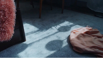 Shadows of plants cast on a carpet near a chair with pink fabric and a peach-colored cloth.