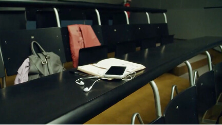 Smartphone and earphones resting on an open notebook on a black table in an empty classroom.
