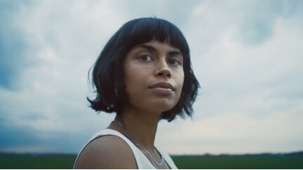 Young woman with short dark hair looking at camera against a cloudy sky background.
