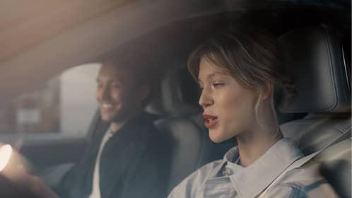 Woman in passenger seat talking while man smiles driving a car during daytime.