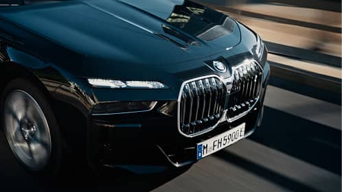 Close-up of front of a black BMW car with large kidney grille and headlights driving on road.