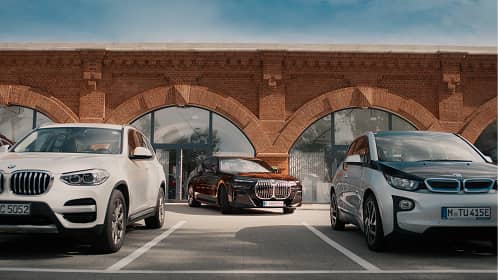 Three BMW cars parked in front of a brick building with arched windows under a blue sky.