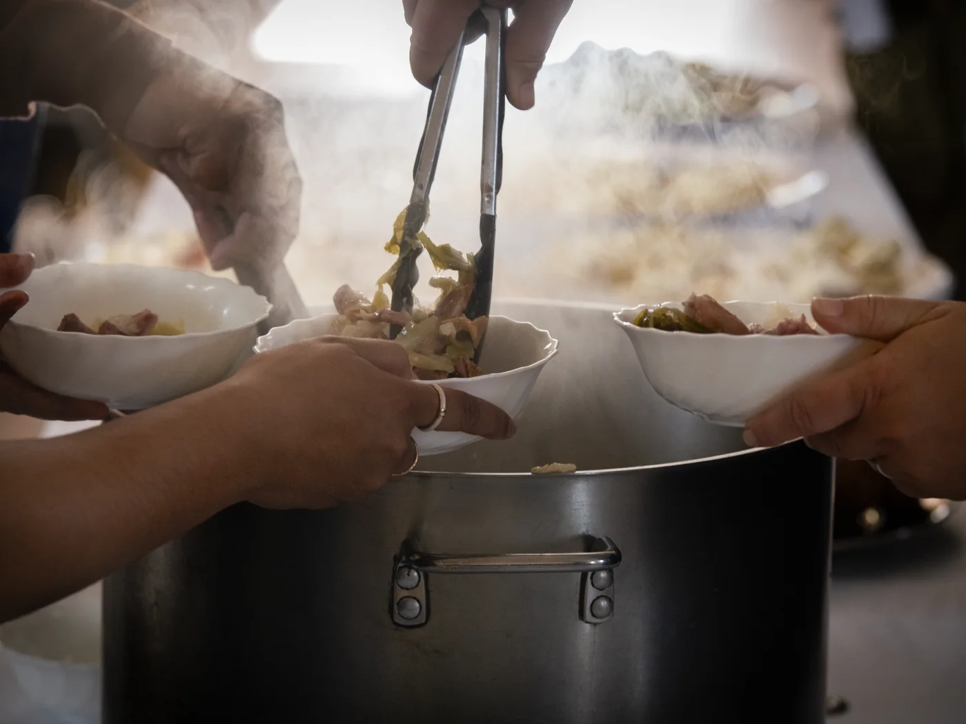 Hands serving kai from pots at a shared table
