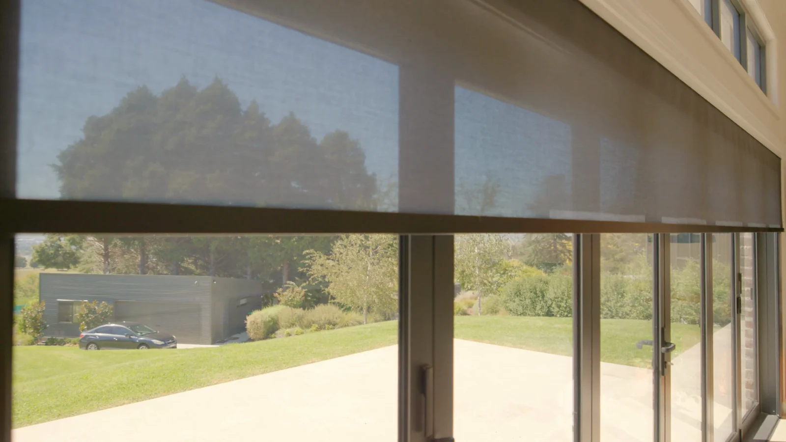 Sunscreen roller blind lowered across a wall of glass with a rural outlook, by Quicksew
