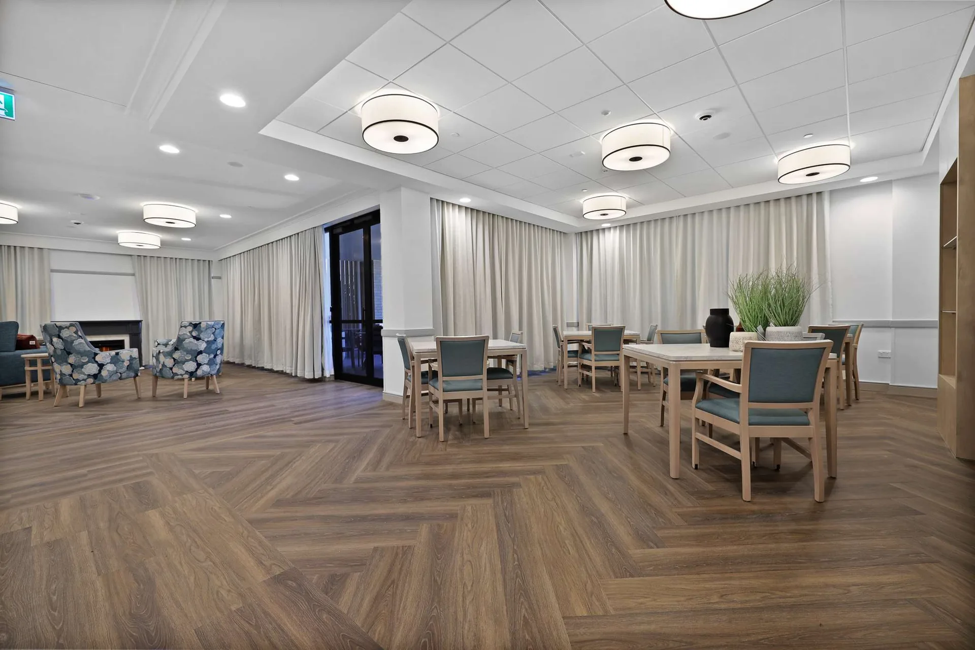 Sheer curtains and floor-length drapes along the windows of an aged-care lounge and dining room