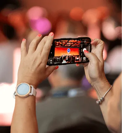 Attendee recording a stage presentation on a smartphone at an event