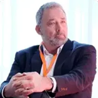 Man in a navy suit and event lanyard speaking during a panel discussion