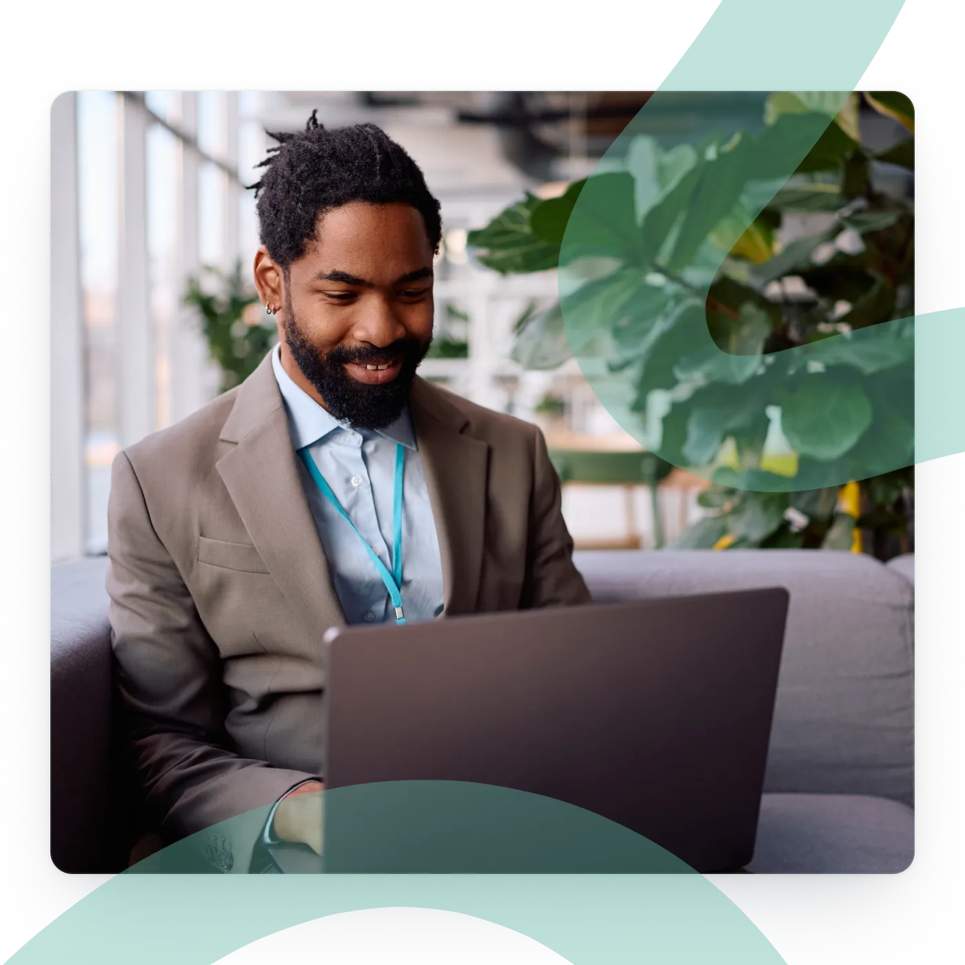 Smiling event professional wearing a lanyard and working on a laptop in a plant-filled lounge