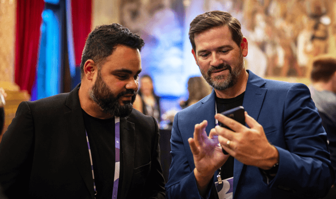 Two conference delegates with lanyards looking at a phone together