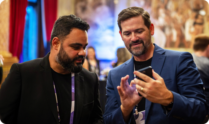 Two event professionals with lanyards looking at a phone together at a conference