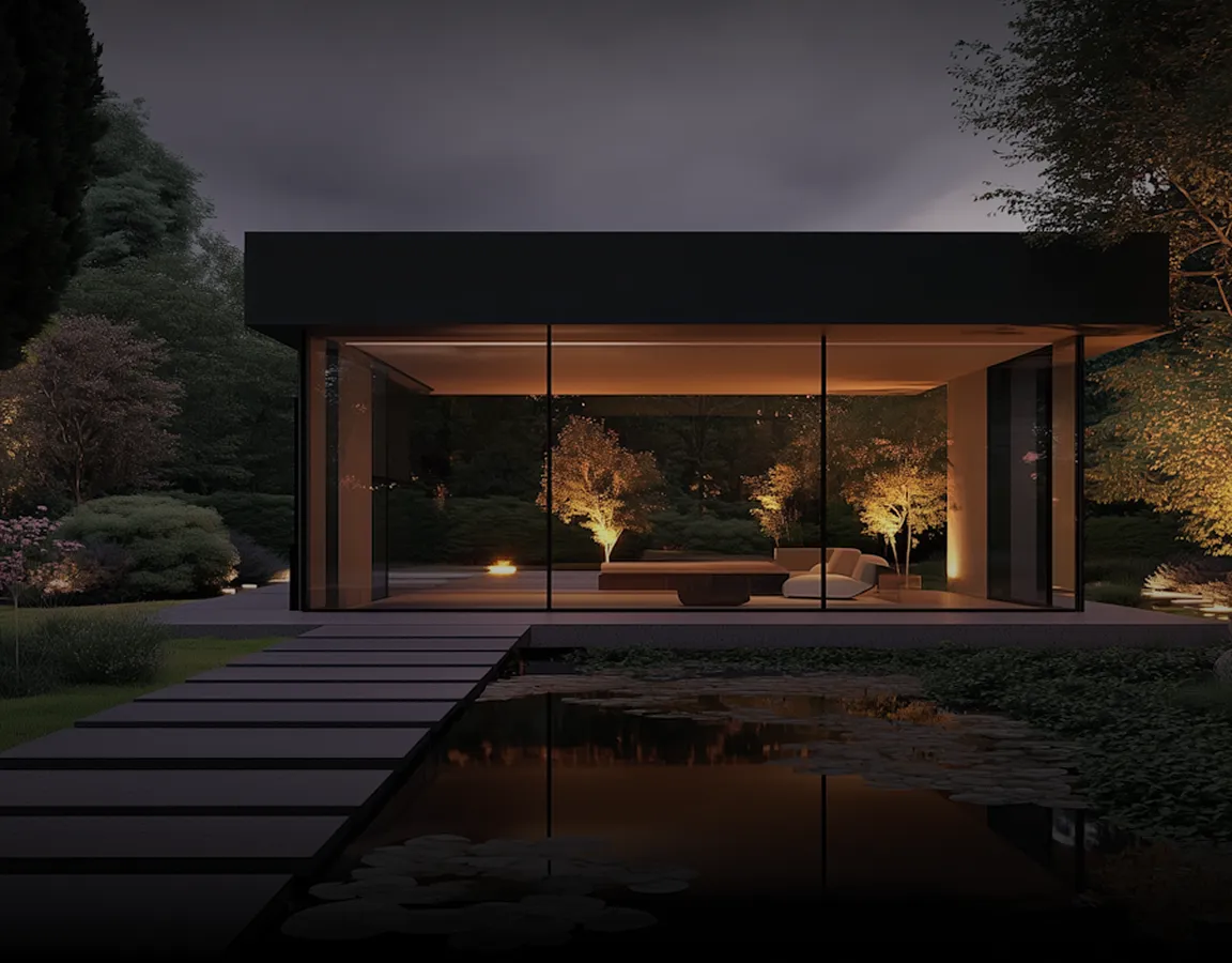 Modern glass pavilion lit warmly at night, surrounded by trees and reflected in a pond with lily pads.