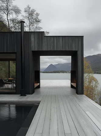 Modern dark wood house deck overlooking lake and mountain under cloudy sky.