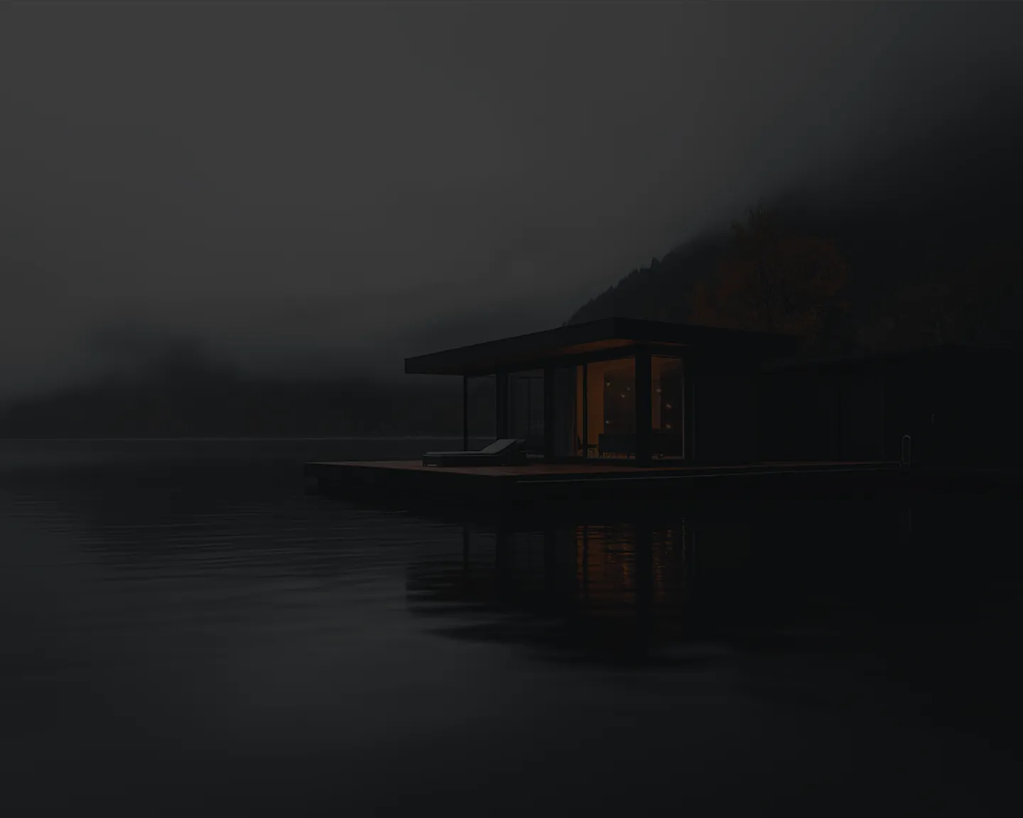 Modern lakeside house with glowing interior light on a dark, foggy night.