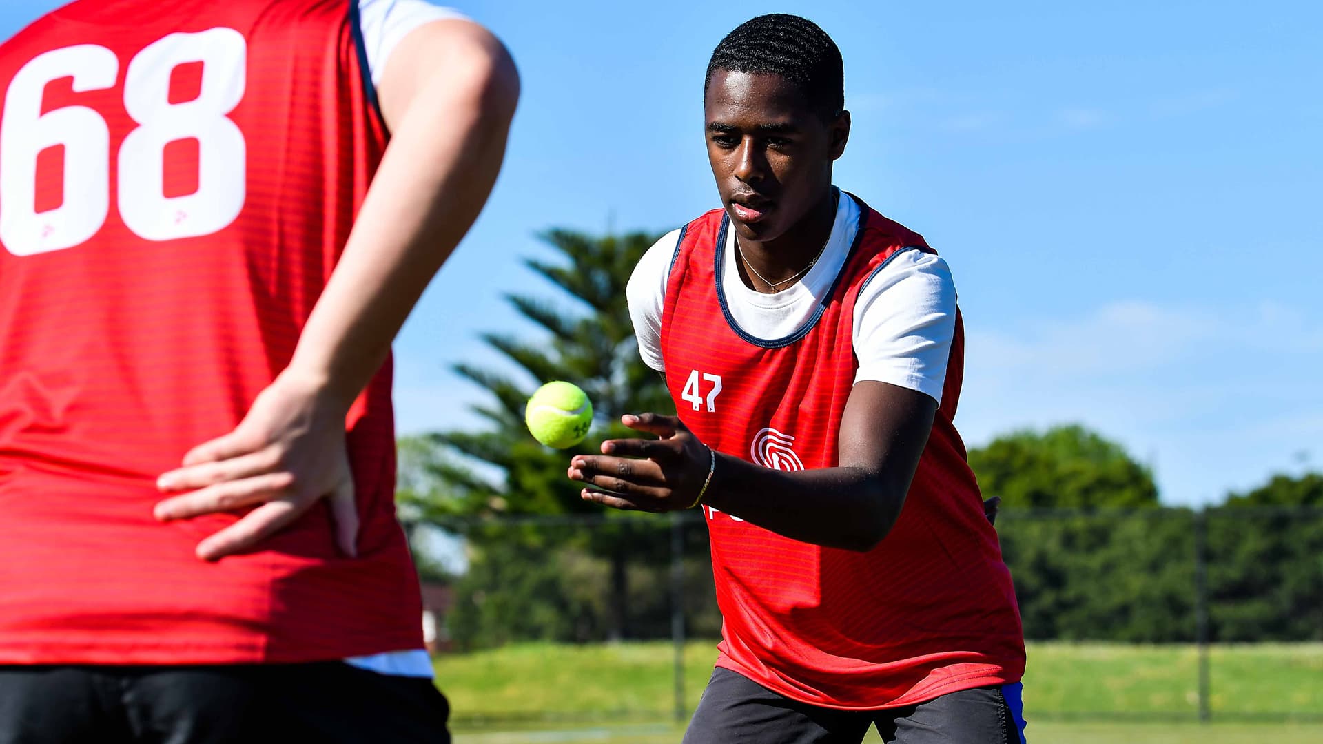 Athletes in red team jerseys during a SportsKey catching and reaction assessment on an outdoor field