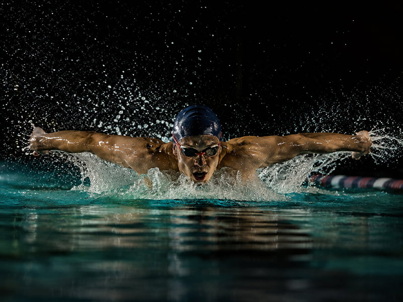 Swimmer in goggles and cap doing butterfly stroke with water splashing around.