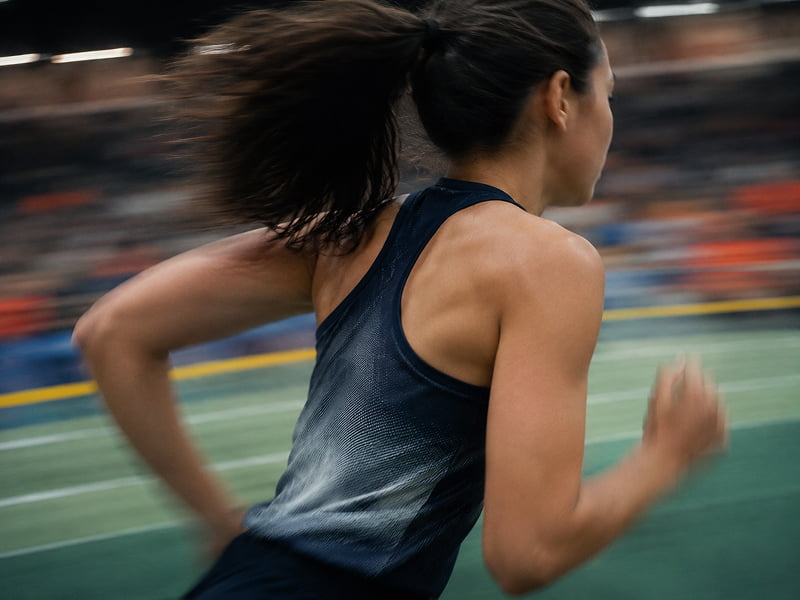 Female athlete with ponytail running fast indoors on a track with blurred background.