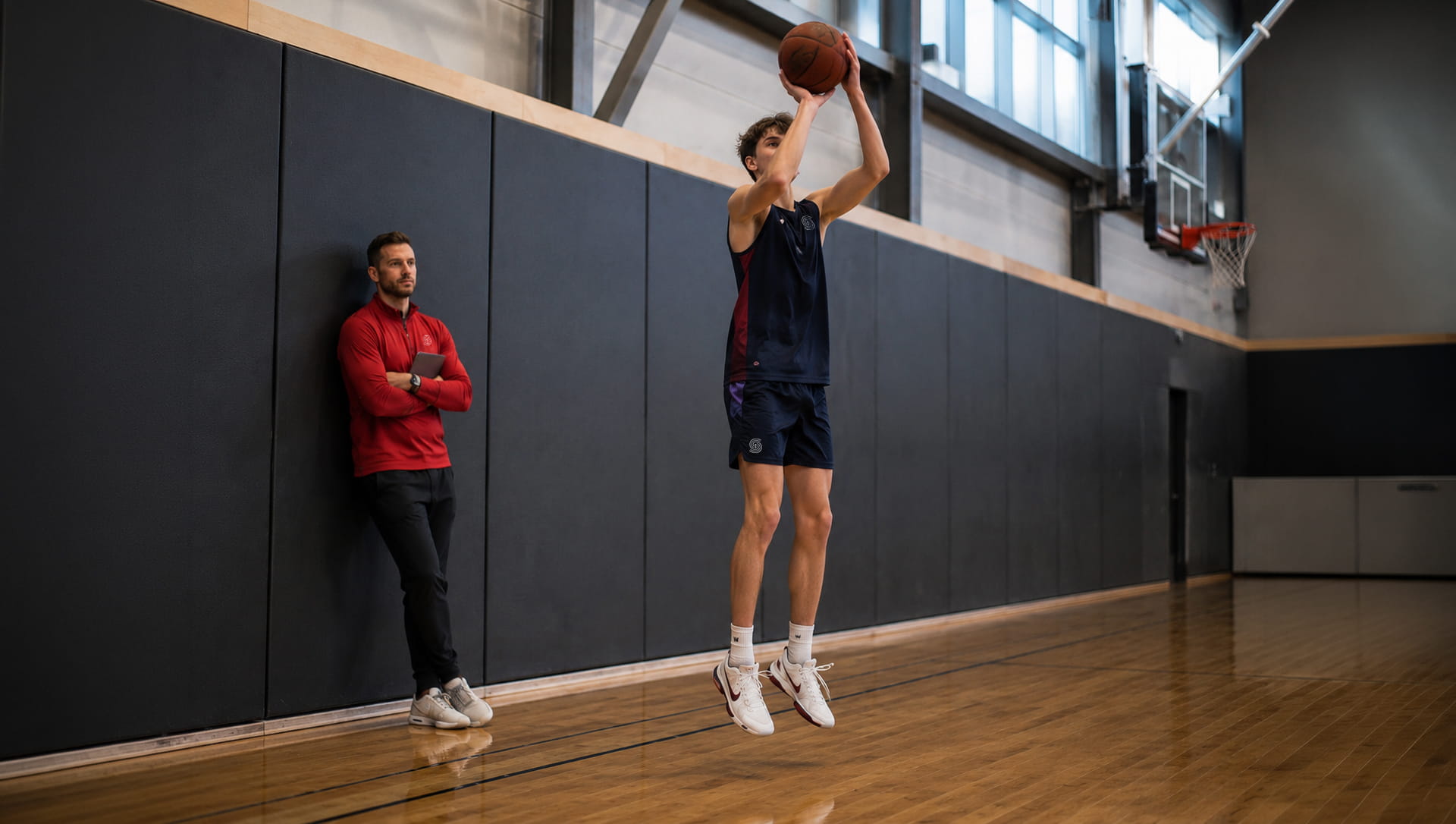 Student athlete shooting a basketball on an indoor court while a coach observes