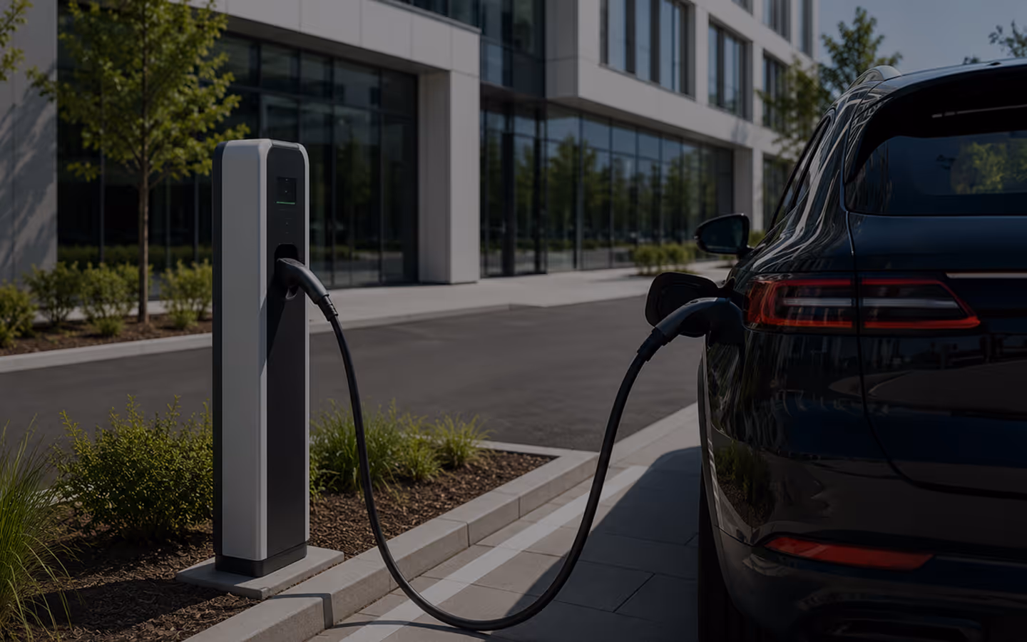 Black electric car charging at a tall outdoor charging station near a modern office building.