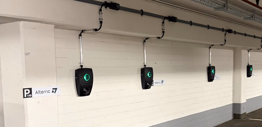 Four black electric vehicle charging stations mounted on a white brick wall in a parking garage.