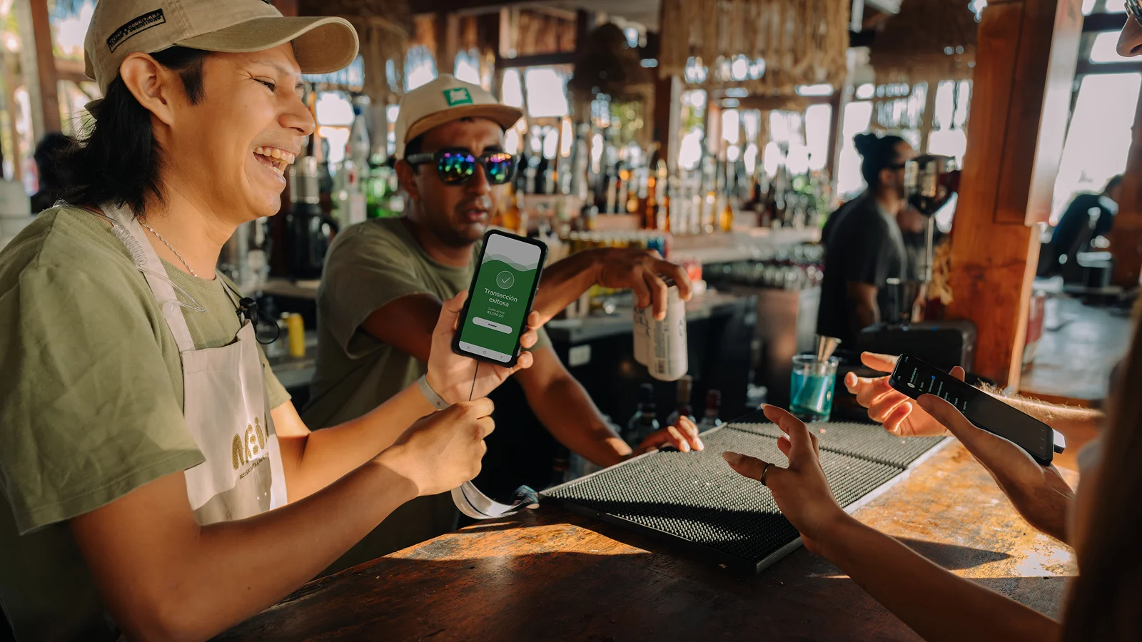 Meseros procesando pago cashless con celular usando la aplicación Billtag en barra de evento en la playa