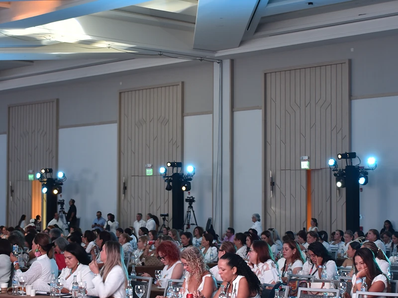 Salón de eventos con invitadas vestidas de blanco durante una celebración corporativa