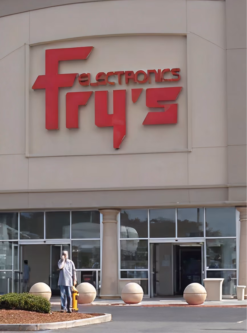 Entrance of Fry's Electronics store with large red sign and person standing near fire hydrant.