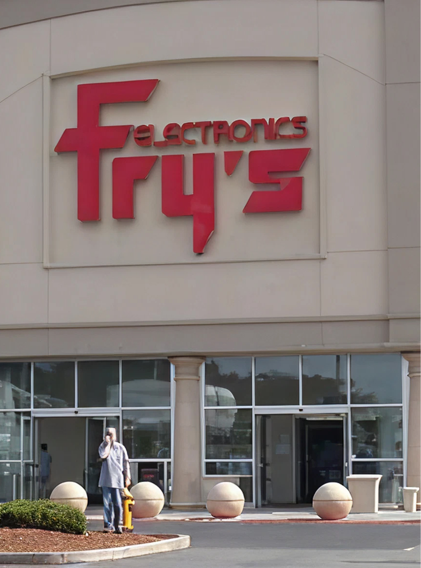 Entrance of Fry's Electronics store with large red sign and person standing near fire hydrant.