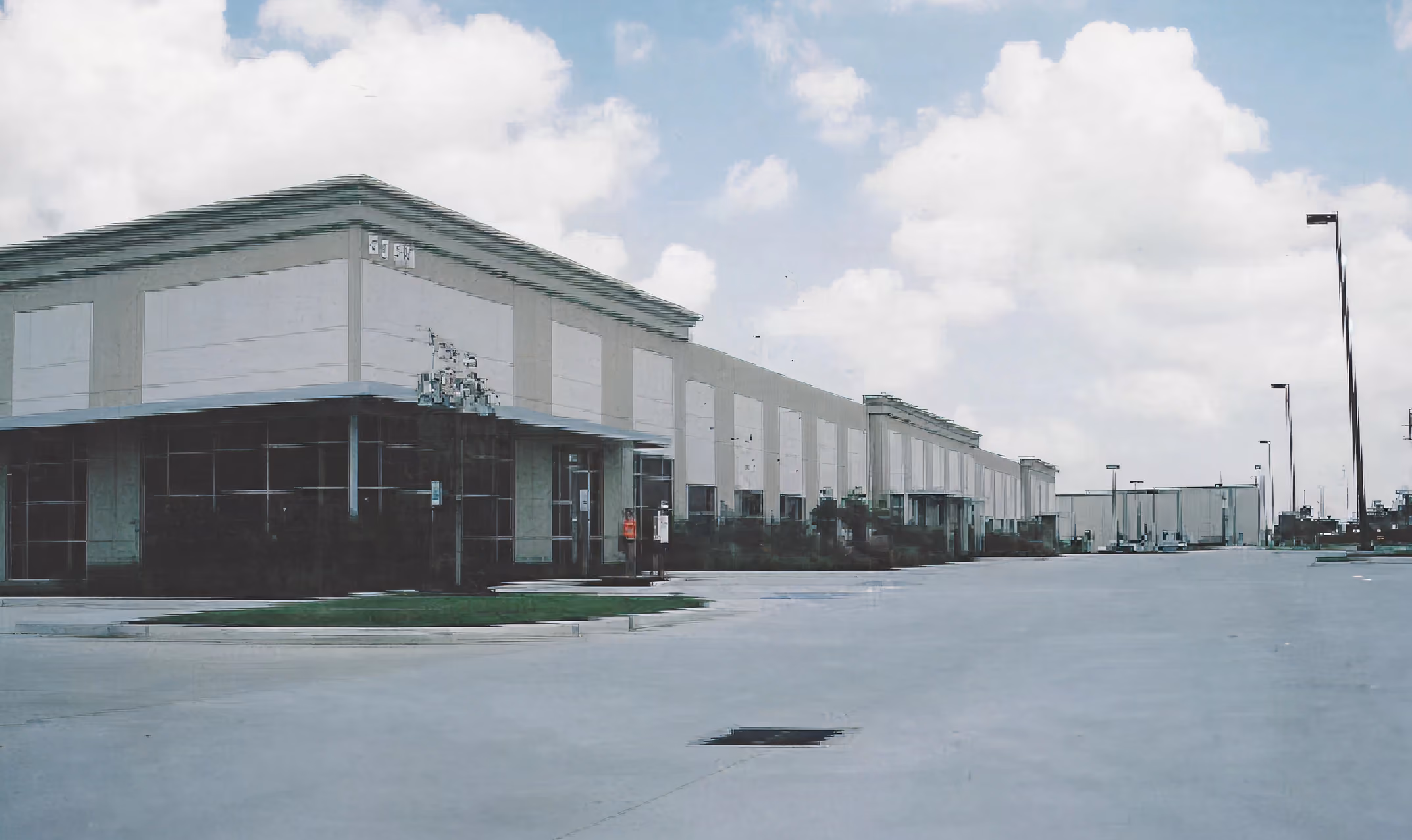 Long, empty industrial warehouse building under a partly cloudy sky with street lamps.