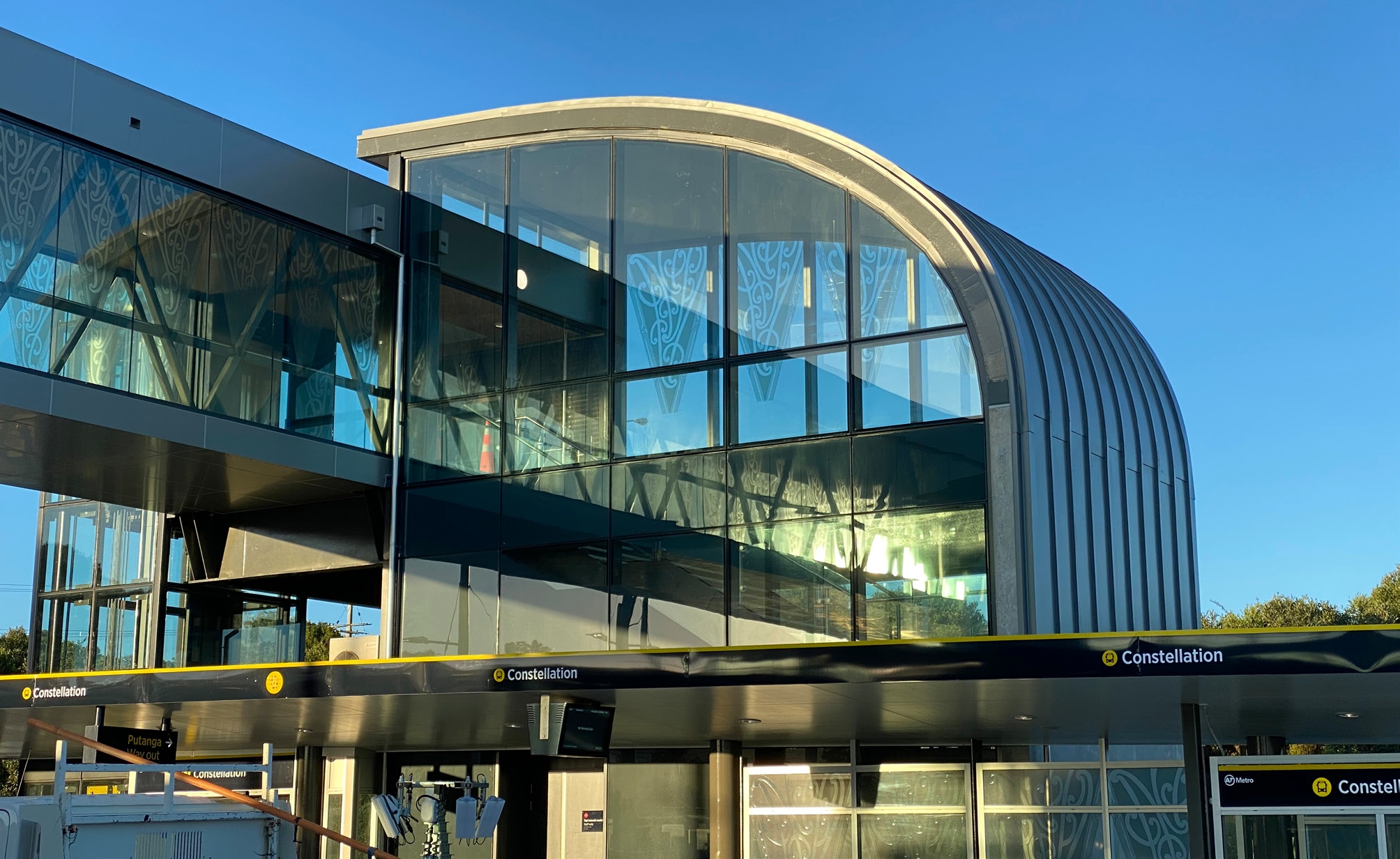 Modern bus station building with glass windows and curved metal roof under clear blue sky.
