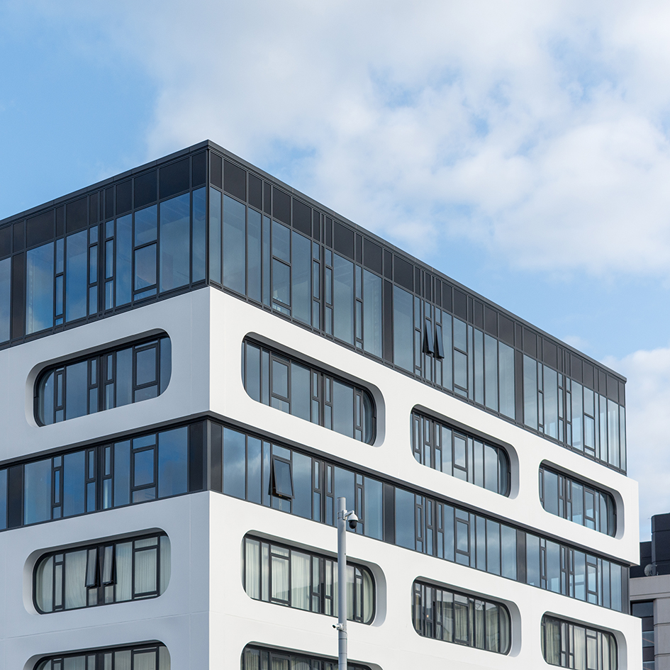 Modern white building with rounded rectangular black-framed windows under a partly cloudy sky.