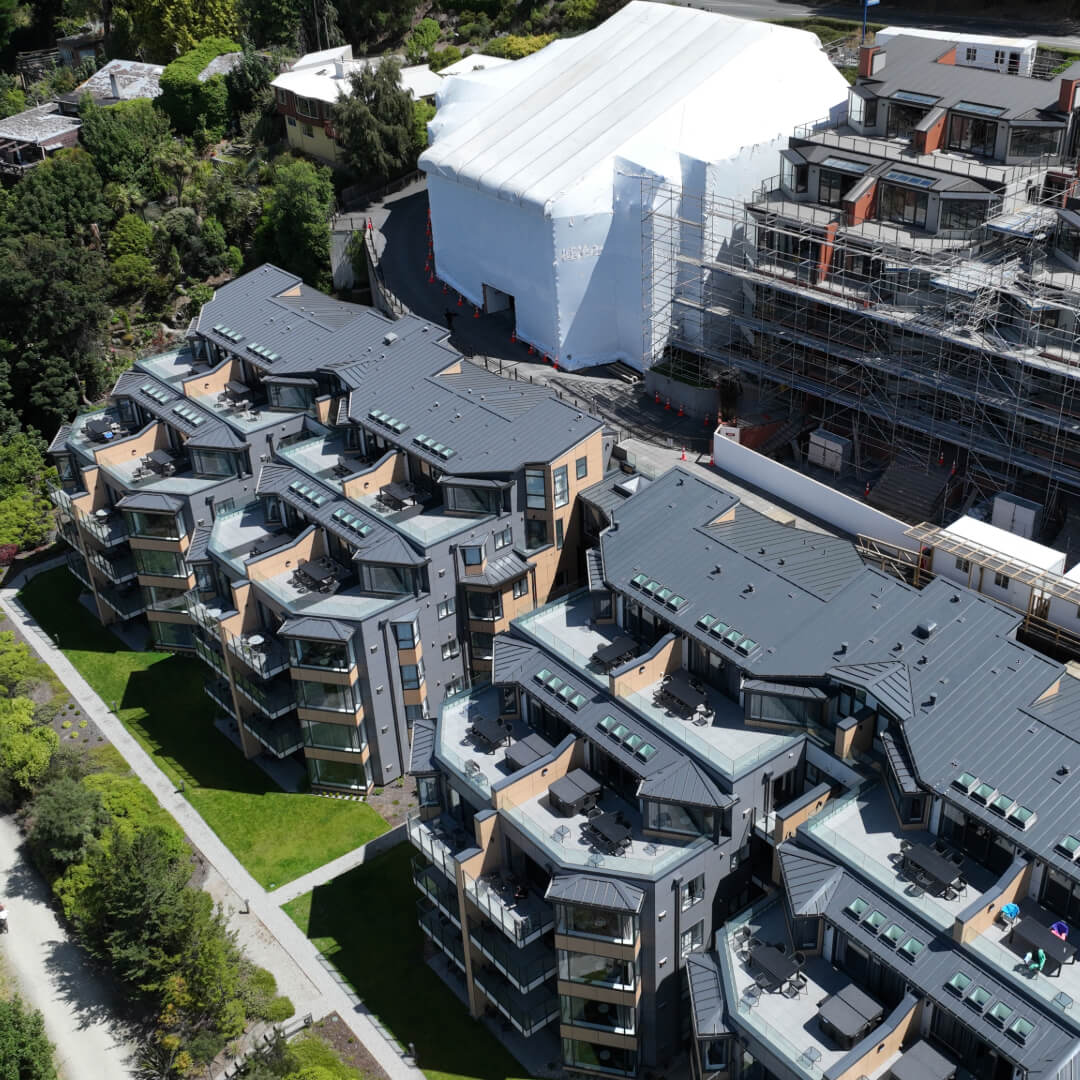 Aerial view of modern residential buildings with grey roofs beside a white covered construction area.