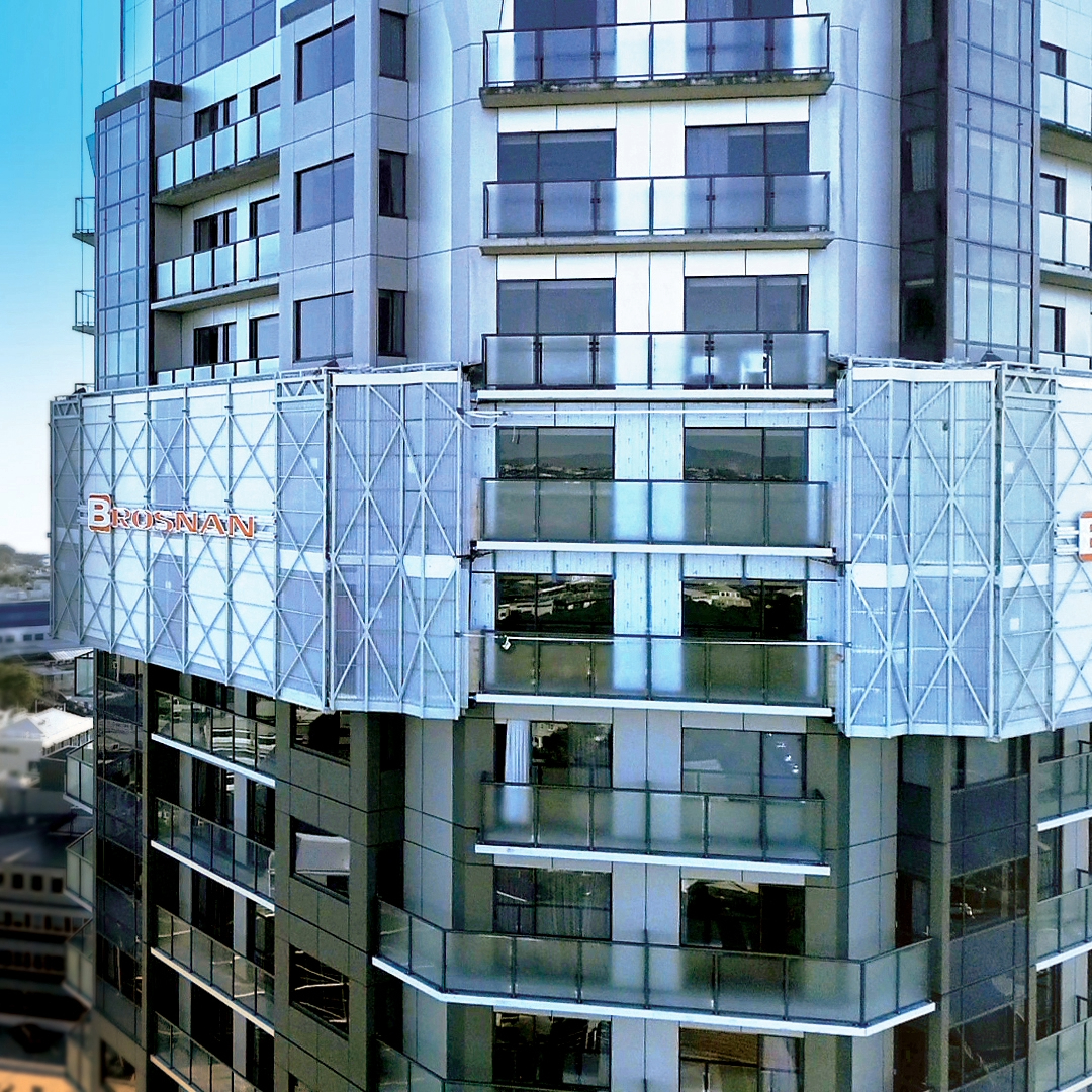 Modern high-rise building with glass balconies and a sign reading Brosnan on the upper floors.