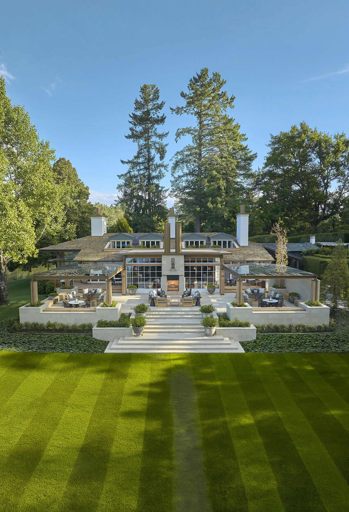Modern house with large patio, outdoor seating areas, fireplace, and a manicured lawn in front.