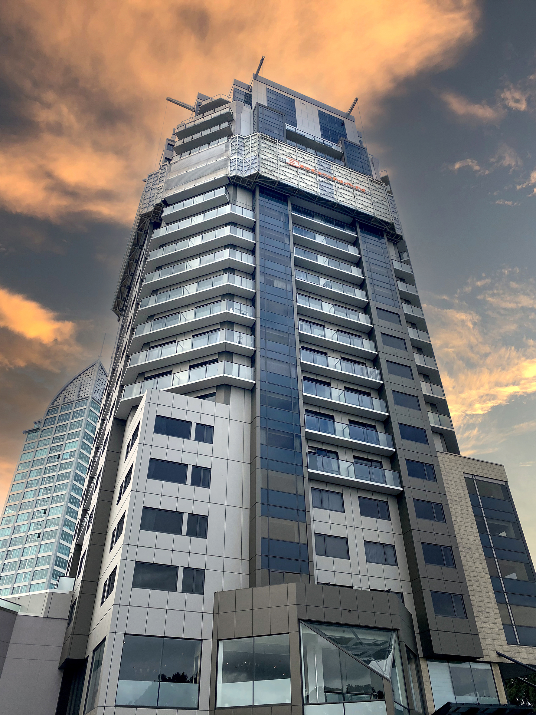 Modern high-rise building with balconies under an orange sunset sky with clouds.
