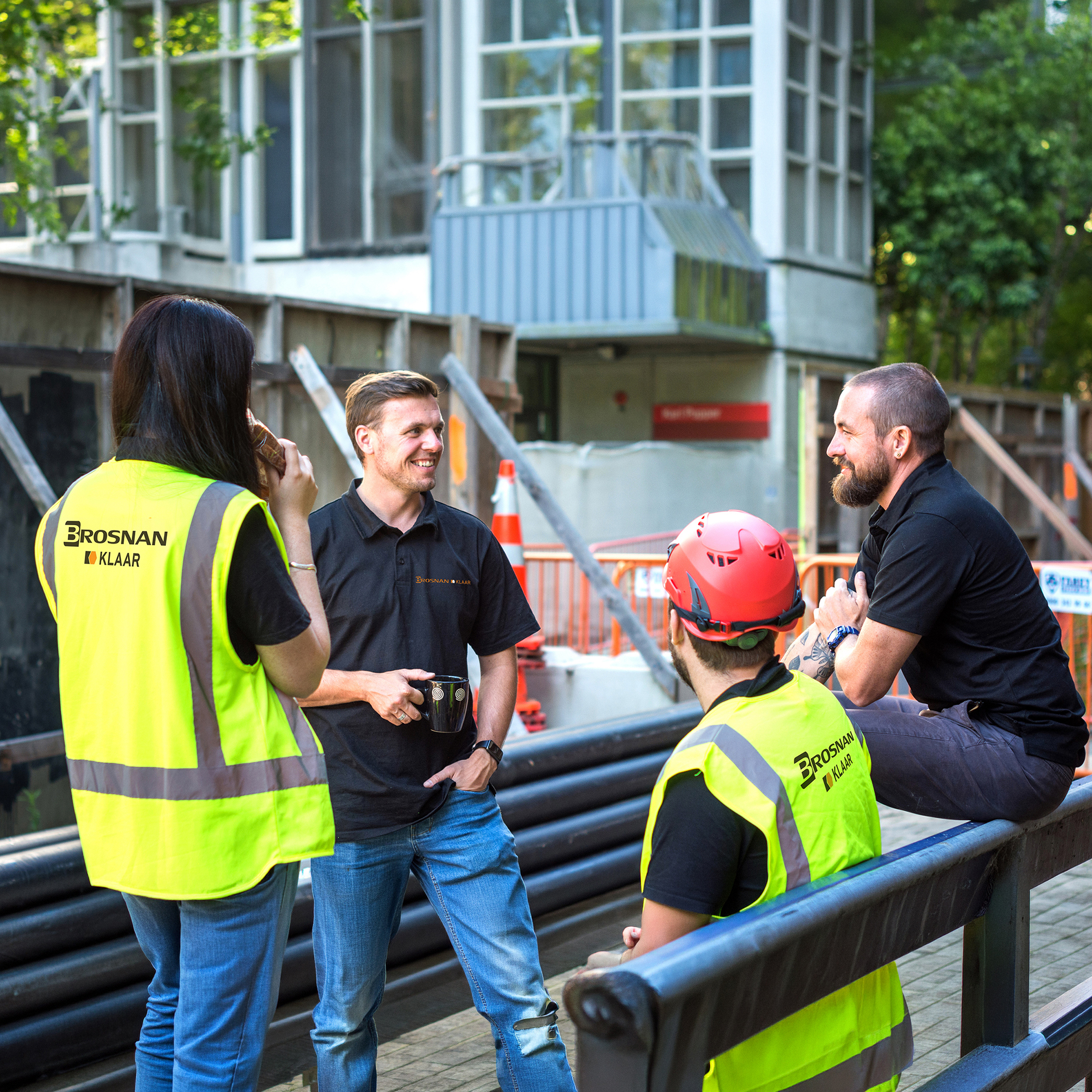 Four construction workers talking during a break, two in yellow vests and one with a red helmet.