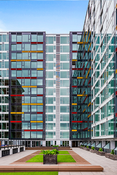 Modern building with glass windows featuring red and yellow accents around a courtyard with greenery and benches.