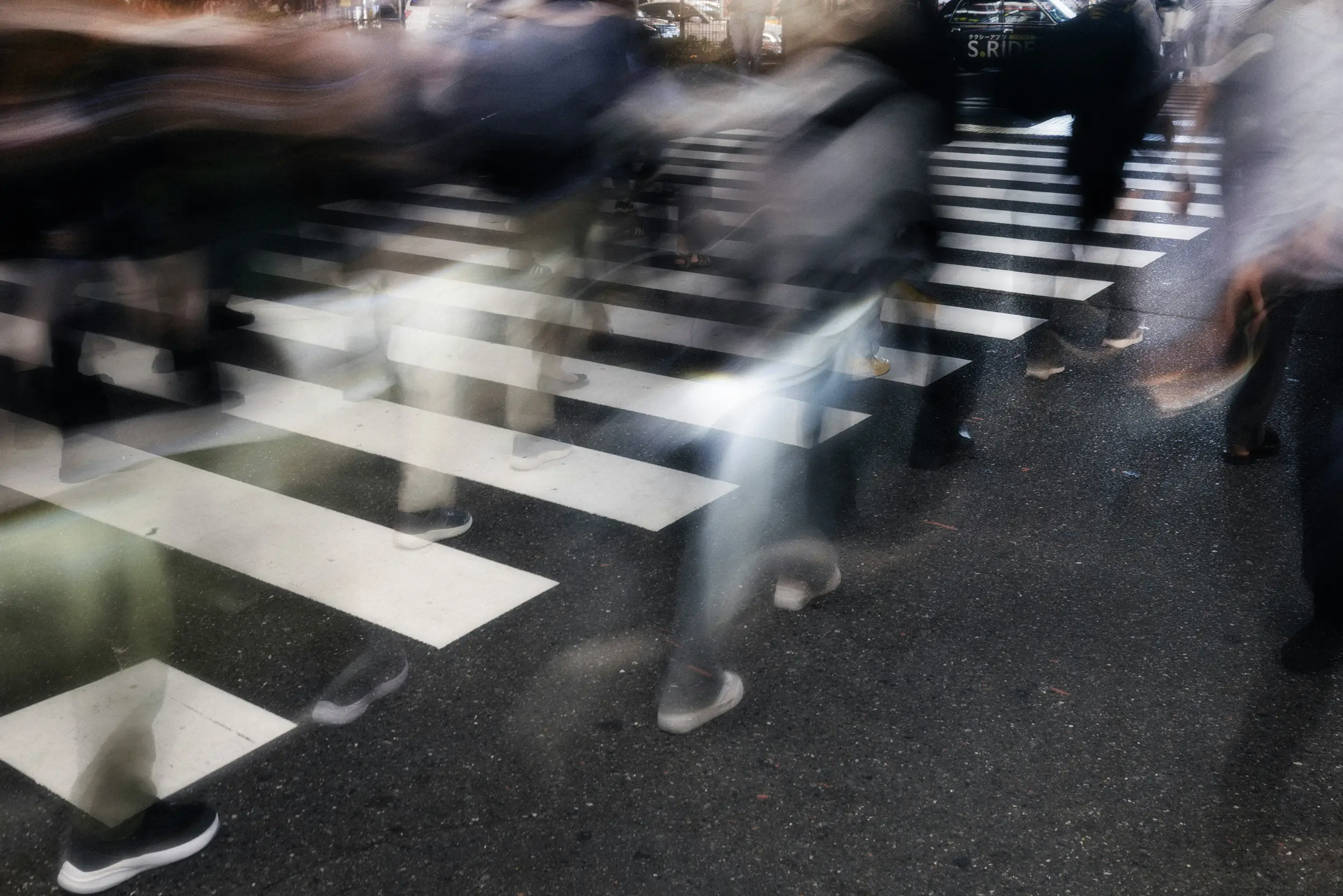 Blurred people walking across a zebra crosswalk on a city street at night.