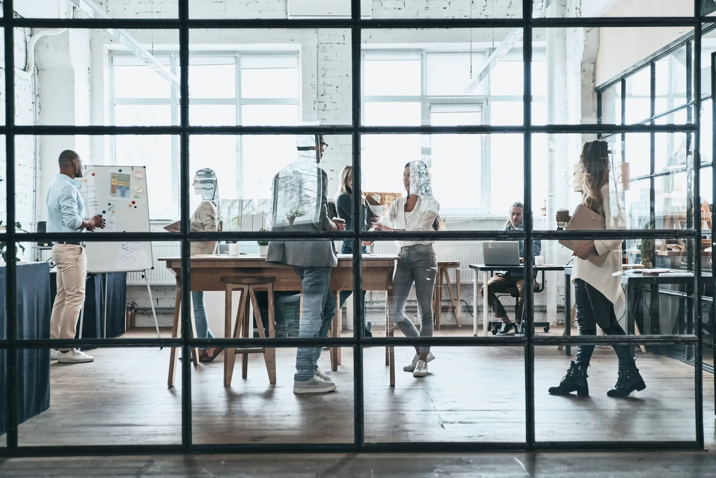 Group of people collaborating in a bright modern office with large windows and glass partitions.