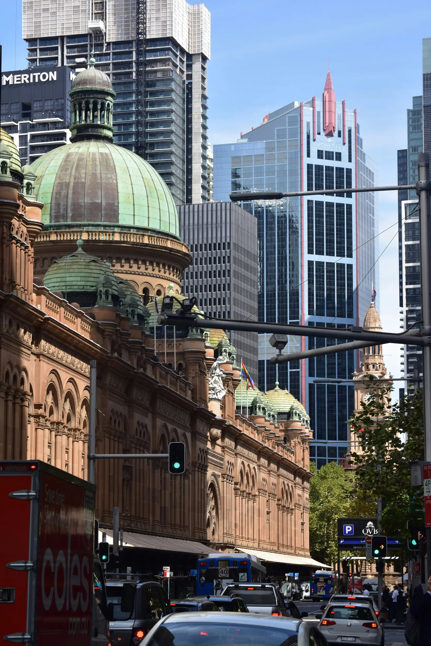 Historic building with green domes and modern skyscrapers behind in a city street with cars and traffic lights.