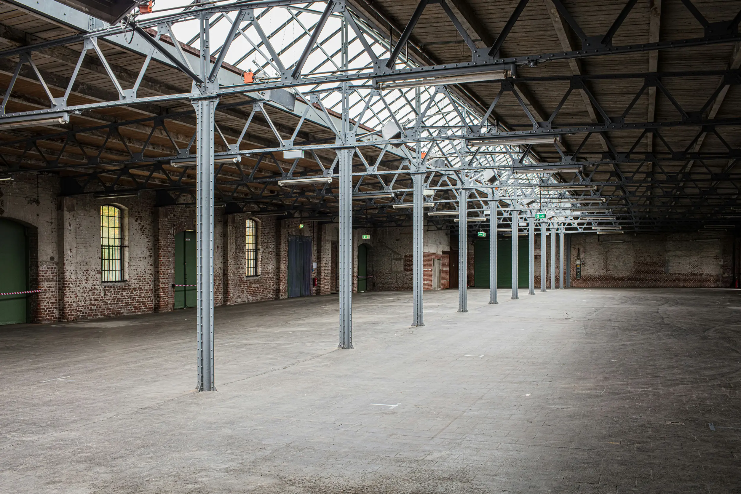 Empty industrial warehouse interior with metal support beams and brick walls under a large skylight roof.