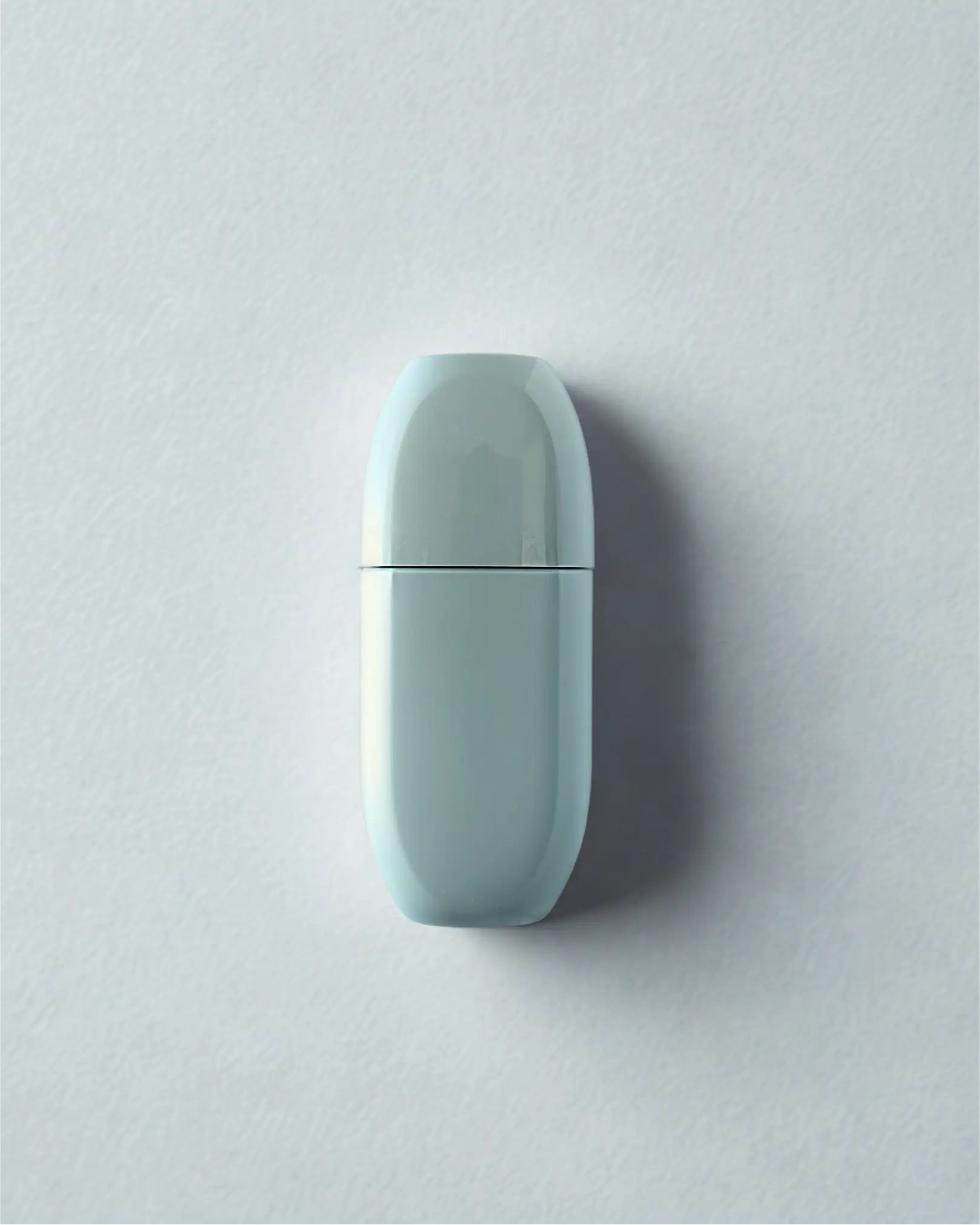 Minimalist matte terracotta cylindrical bottle placed on a concrete pedestal with diagonal shadows.